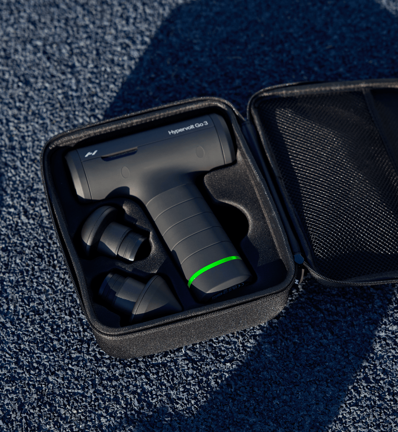 Hypervolt Go 3 massage device with green battery light in a black case on a textured blue surface