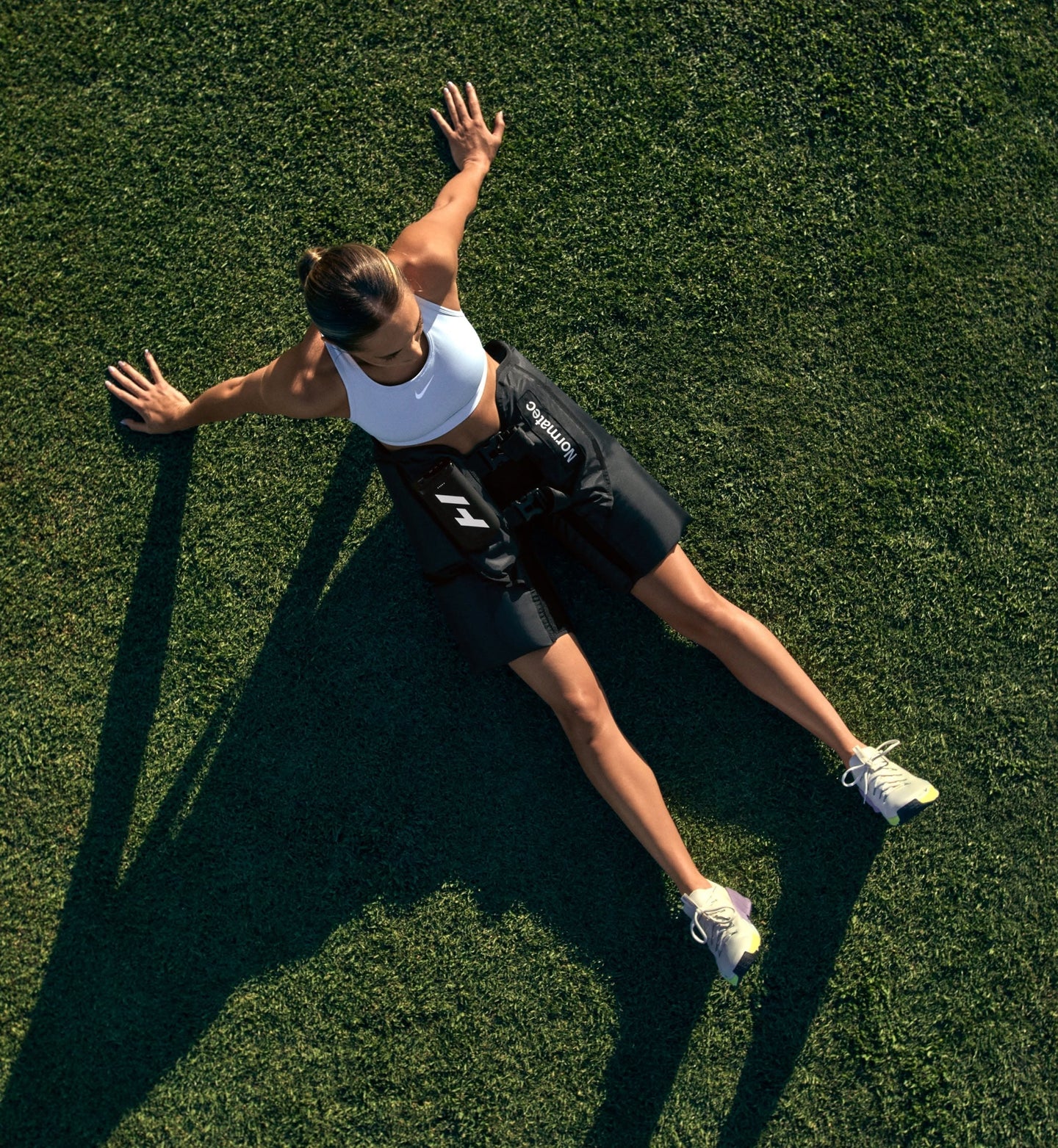 A person sitting down on a grassy field with arms outstretched wearing normatec elite hips
